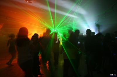 Personnes dansant dans une salle sombre éclairée par des faisceaux lumineux verts et orange.