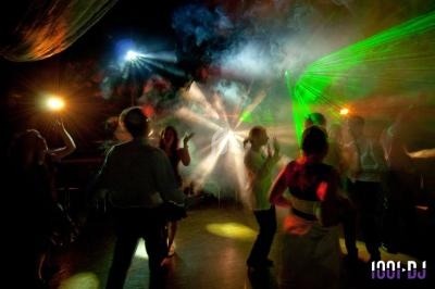 Personnes dansant sous des jeux de lumières colorées et des effets de fumée dans une ambiance festive.