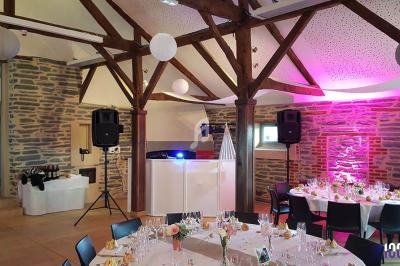 Salle de réception décorée avec des tables dressées, un espace DJ éclairé et des murs en pierre apparente.
