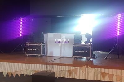 Scène avec éclairage violet, équipement de DJ et table lumineuse marquée ’100% DJ’ dans une salle de réception.