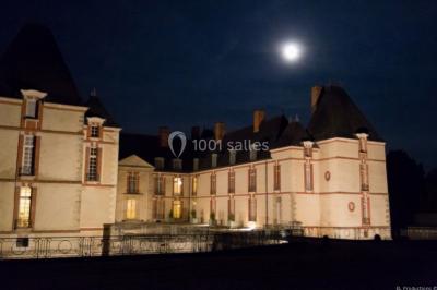 Château éclairé sous un ciel nocturne avec une pleine lune visible en arrière-plan.
