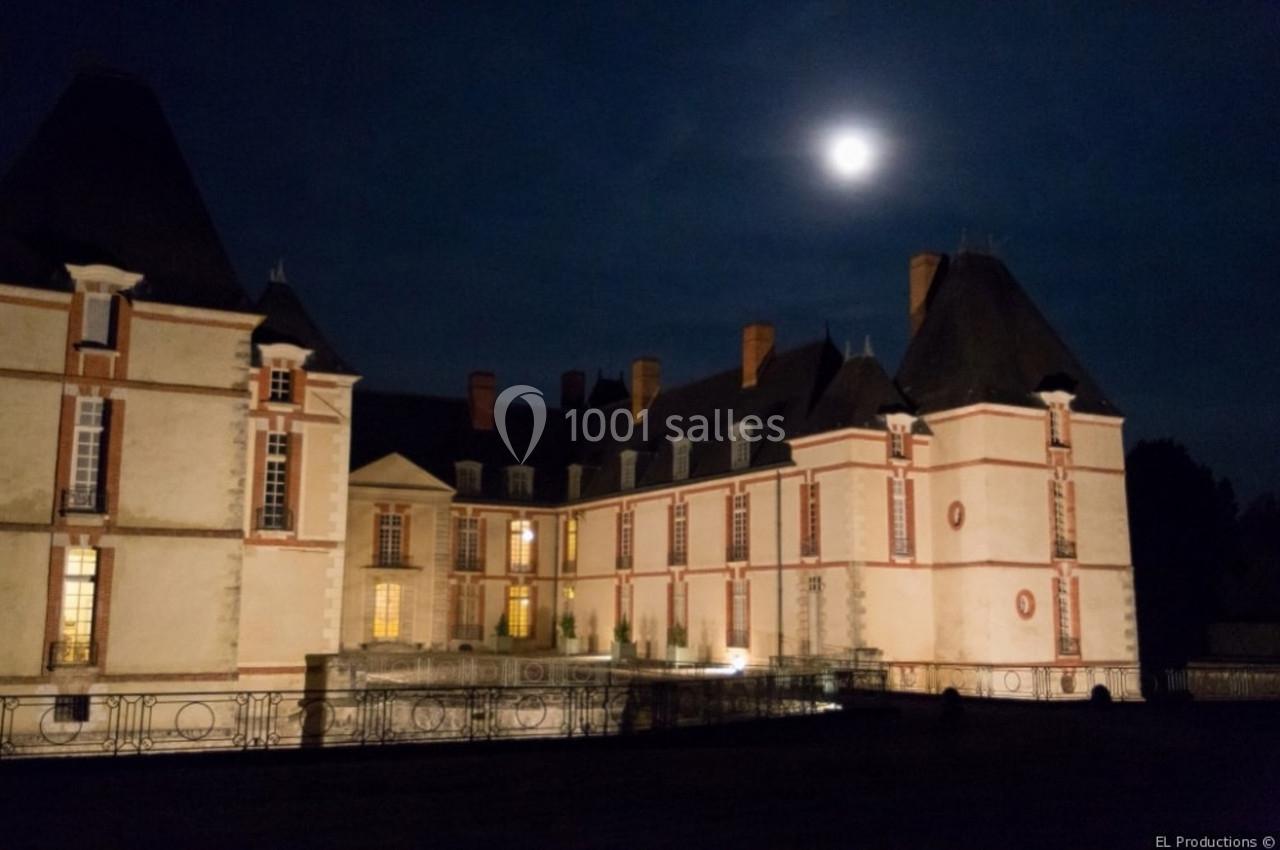 Château éclairé sous un ciel nocturne avec une pleine lune visible en arrière-plan.