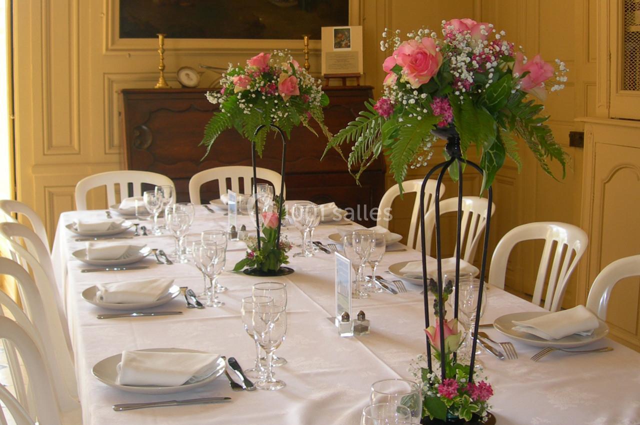 Table dressée avec nappes blanches, vaisselle élégante et centres de table fleuris dans une salle lumineuse.