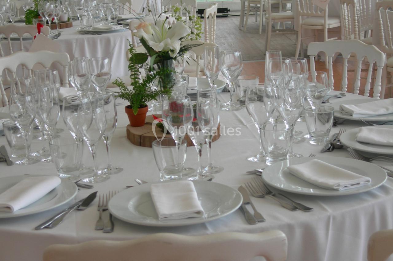 Tables élégamment dressées avec nappes blanches, verres, assiettes, serviettes pliées et décorations florales.
