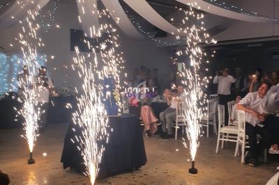 Des jets d'étincelles entourent une table décorée sous des drapés blancs lors d'une fête en intérieur.