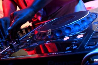 Un DJ ajuste les commandes sur une table de mixage éclairée par des lumières colorées.