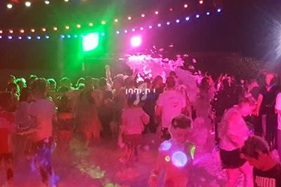 Groupe de personnes dans une fête nocturne avec mousse, éclairages colorés et ambiance festive.