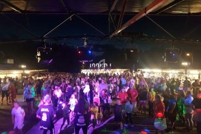 Foule rassemblée en soirée sous un chapiteau éclairé, avec des stands en arrière-plan et des lumières colorées.