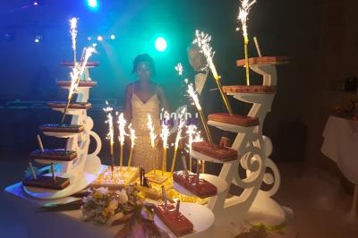 Un couple en tenue de mariage devant une pièce montée éclairée par des cierges étincelants dans une salle sombre.