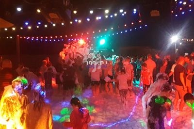 Des personnes dansent sous des lumières colorées lors d'une fête avec de la mousse au sol.