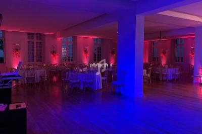 Salle de réception décorée avec des lumières roses, tables dressées et chaises disposées autour.