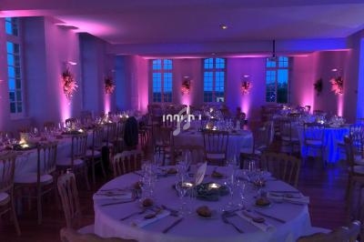 Salle de réception décorée avec des tables rondes dressées, éclairage tamisé aux tons roses et violets.