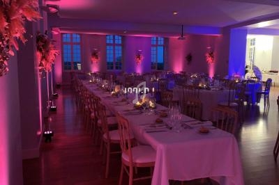 Salle de réception décorée avec des tables dressées, éclairage tamisé rose et violet, ambiance élégante.