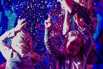Des enfants souriants jouent sous une pluie de confettis lumineux dans une ambiance festive et colorée.