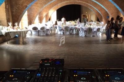 Salle voûtée en briques aménagée pour un événement, avec tables dressées et matériel de DJ au premier plan.