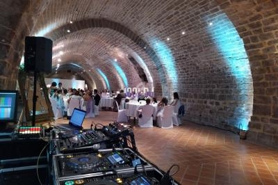 Salle voûtée en pierre éclairée, aménagée pour un événement avec tables dressées et matériel de DJ au premier plan.