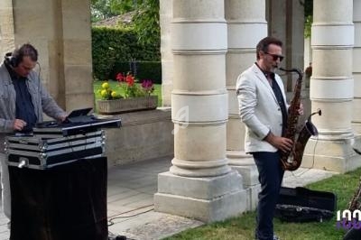 Un DJ mixe sur une console pendant qu'un saxophoniste joue devant des colonnes dans un jardin.