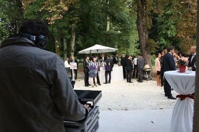 Un DJ anime un événement en plein air avec des invités rassemblés près de tables et d'un parasol dans un parc.