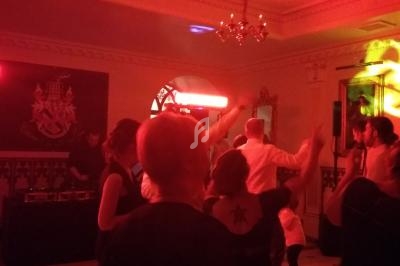 Personnes dansant sous des lumières rouges dans une salle décorée avec des éléments classiques et un blason au mur.