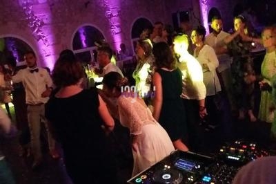 Des invités dansent dans une salle éclairée par des lumières colorées, avec une table de mixage au premier plan.