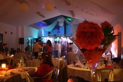 Salle décorée avec des tables dressées, des convives assis et debout, éclairage tamisé et ambiance festive.