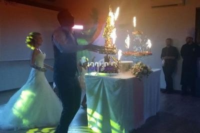 Un couple de mariés observe un serveur apportant un gâteau illuminé de feux d'artifice dans une salle de réception.