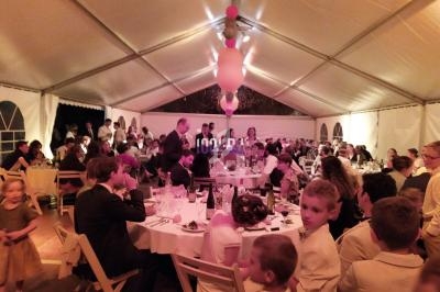 Des invités assis et debout dans une grande tente éclairée, décorée pour une réception en soirée.