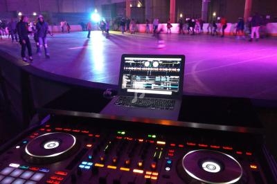 Console de DJ en premier plan avec un ordinateur portable, et une piste de roller éclairée en arrière-plan.