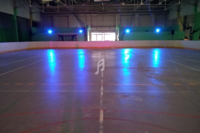 Patinoire intérieure vide avec éclairage bleu, lignes marquées au sol et un but visible en arrière-plan.