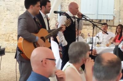 Un groupe de musiciens joue devant des invités assis lors d'un événement en extérieur près d'un mur en pierre.