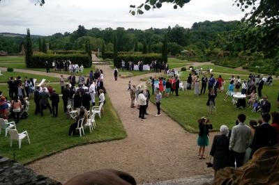Groupe de personnes rassemblées dans un jardin avec pelouse, allées en gravier et arbres en arrière-plan.