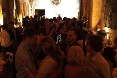Personnes dansant et discutant dans une salle éclairée, avec un plafond en bois et un lustre central.