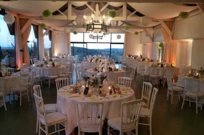 Salle de réception décorée avec des tables rondes dressées, éclairage chaleureux et vue sur l'extérieur.