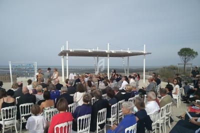 Cérémonie en plein air avec des invités assis face à un couple sous une pergola, près de la mer.