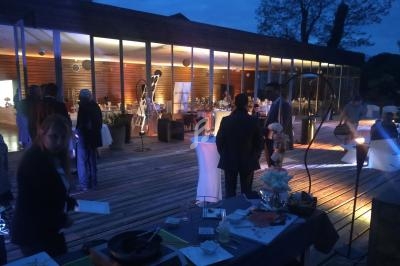 Personnes rassemblées en soirée sur une terrasse éclairée, devant une salle vitrée avec décoration lumineuse.
