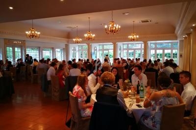 Salle de réception lumineuse avec des invités assis à des tables rondes, décorée de lustres et grandes fenêtres.