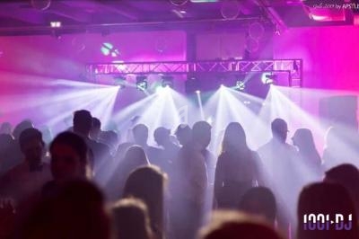 Personnes dansant dans une salle éclairée par des projecteurs colorés et des jeux de lumière.