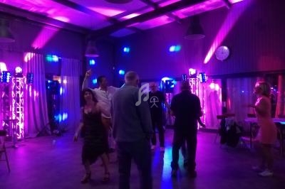 Des personnes dansent dans une salle éclairée par des lumières colorées, avec des équipements audio visibles en arrière-plan.