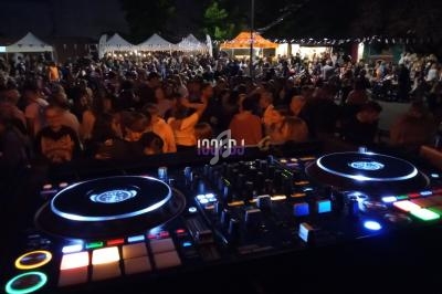 Vue d'une foule lors d'un événement en plein air, avec une table de mixage éclairée au premier plan.