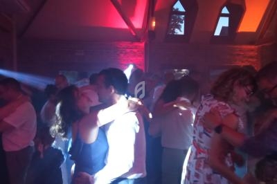 Des couples dansent dans une salle faiblement éclairée avec des lumières colorées et une ambiance festive.