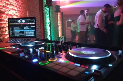 Console de DJ avec platines et ordinateur en premier plan, éclairages colorés et personnes dansant en arrière-plan.