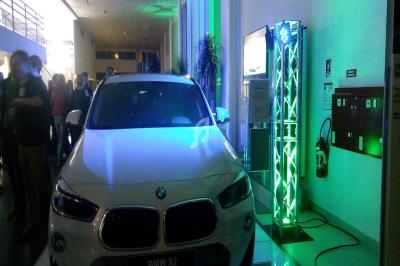 Voiture blanche BMW X2 exposée dans un espace intérieur, éclairée par des lumières vertes et bleues.