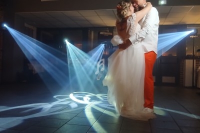Un couple danse dans une salle éclairée par des projecteurs lumineux, entouré d'une ambiance festive.