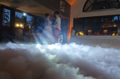 Un couple danse au milieu d'une piste entourée de fumée, dans une salle éclairée par des lumières tamisées.