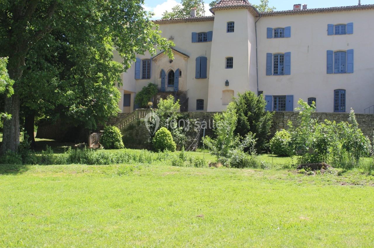Façade d'un grand bâtiment ancien avec volets bleus, entouré d'arbres et d'un jardin verdoyant.