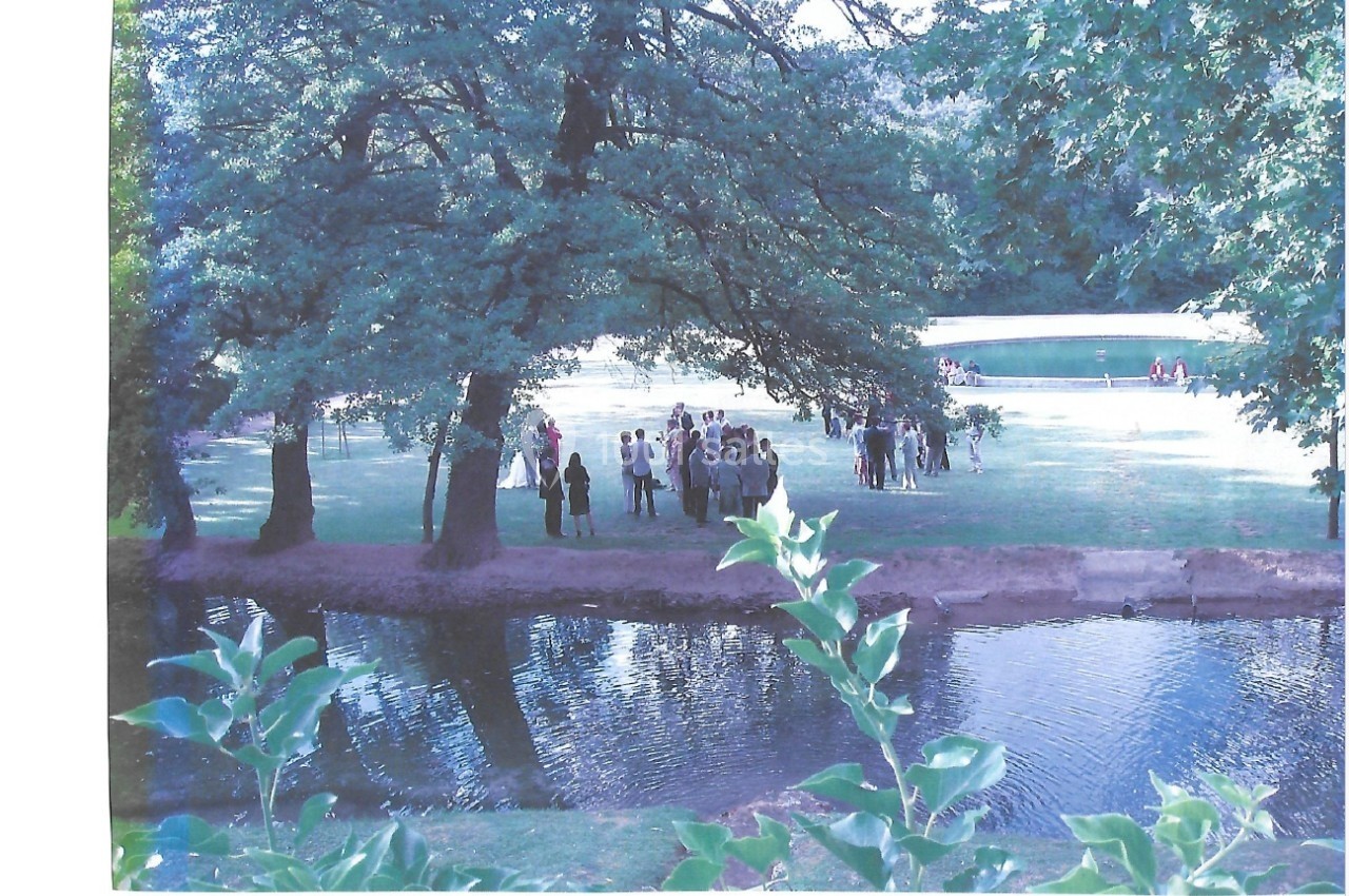 Groupe de personnes rassemblées dans un parc verdoyant près d'un étang, entouré d'arbres et de pelouse.