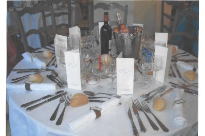 Table dressée pour un repas avec nappes blanches, couverts, verres, menus, pains, bouteille de vin et seau à glace.