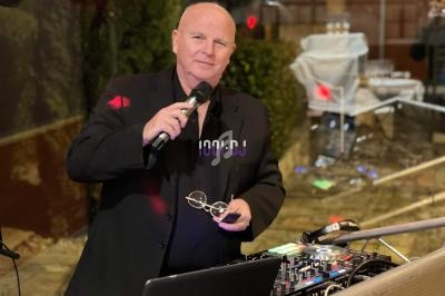 Homme tenant un micro devant une table de mixage lors d'un événement en extérieur, éclairage tamisé.