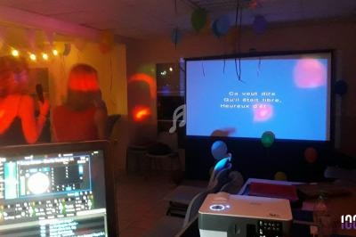 Deux personnes chantent devant un écran de karaoké dans une salle décorée de ballons et éclairée par des lumières colorées.