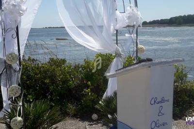 Arche décorée de fleurs blanches et pupitre face à un paysage côtier avec végétation et eau en arrière-plan.